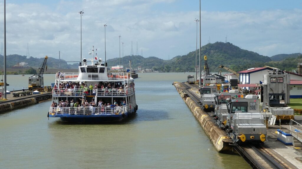 Buque de carga saliendo de puerto en Panama con grúas y contenedores al fondo, representando transporte marítimo.